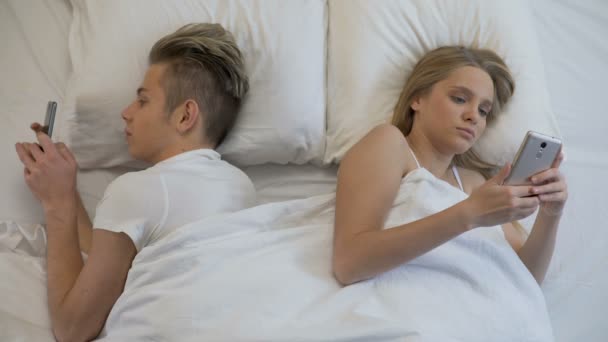 Couple lying back to back in bed with smartphones, social networks, ignore - Imágenes, Vídeo
