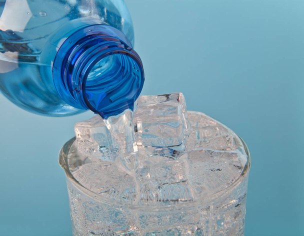 Flowing water in a glass with ice from a bottle on a blue backgr - Фото, зображення