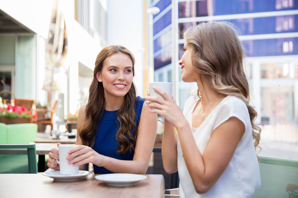 smiling young women drinking coffee at street cafe - Photo, image