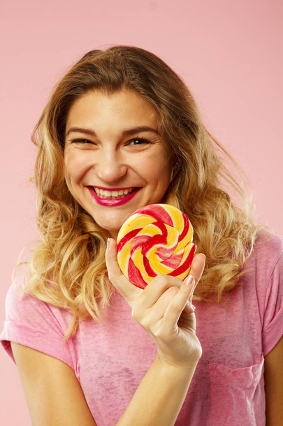 Portrait of a happy pretty girl holding sweet candy over pink ba - 写真・画像