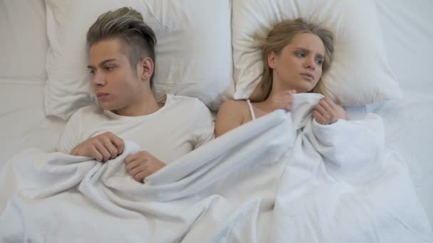 Upset young couple lying in bed, angrily pulling blanket, conflict in relations - Footage, Video