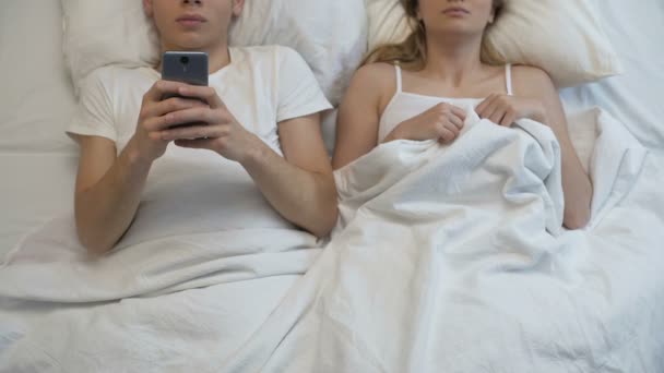 Boyfriend playing smartphone games in bed, ignoring girlfriend, couple problem - Materiał filmowy, wideo