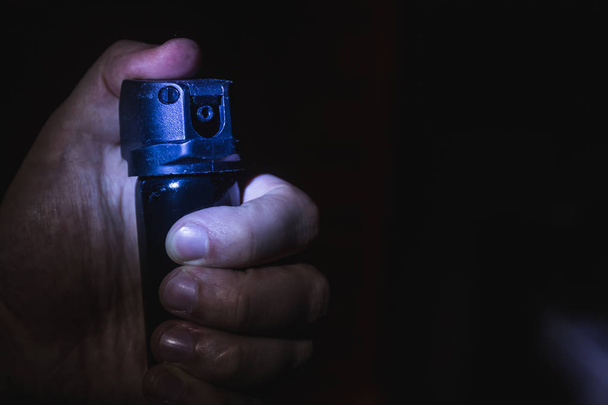 una mano de hombre sostiene un gas pimienta aerosol en la oscuridad, un respaldo negro
 - Foto, Imagen