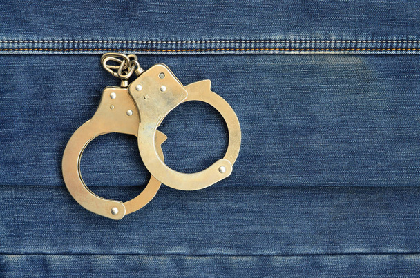 Поліцейські сталеві наручники лежать на фоні темно-синіх джинсів
 - Фото, зображення