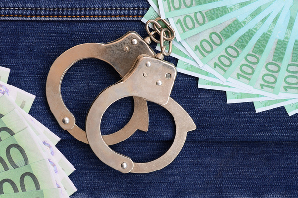 The fan of a lot of euro bills and police handcuffs is on a dark denim surface. Background image - Fotoğraf, Görsel