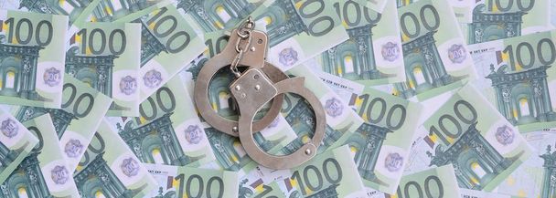 Politie handboeien ligt op een aantal groene monetaire denominaties van 100 euro. Een heleboel geld vormt een oneindige heap - Foto, afbeelding
