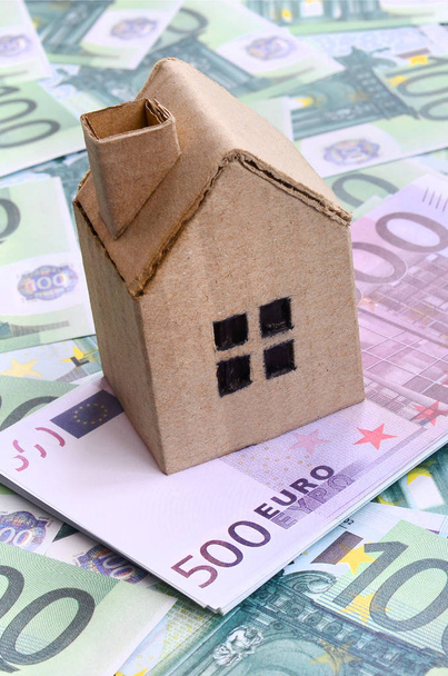 Klein speelgoed huis ligt op een set van groene monetaire denominaties van 100 euro. Een heleboel geld vormt een oneindige heap - Foto, afbeelding