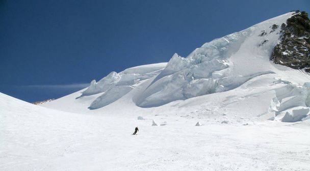 skieur de fond descendant un immense glacier alpin par une belle journée d'hiver avec des séracs de glace suspendus derrière lui
 - Photo, image