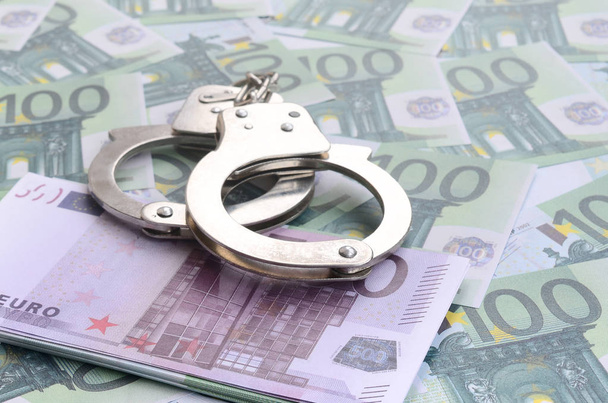 Αστυνομικό ψέματα χειροπέδες σε ένα σύνολο πράσινο νομισματική ονομαστικές αξίες των 100 ευρώ. Πολλά χρήματα σχηματίζει μια άπειρη σωρού - Φωτογραφία, εικόνα