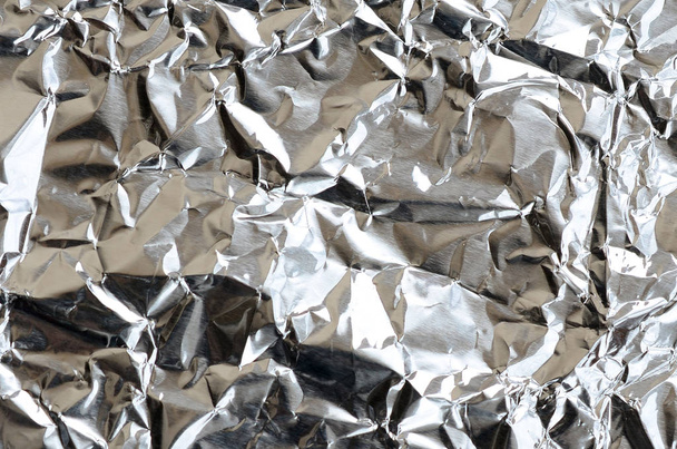 Thin wrinkled sheet of crushed tin aluminum silver foil background with shiny crumpled surface for texture - Foto, Imagen