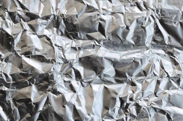 Thin wrinkled sheet of crushed tin aluminum silver foil background with shiny crumpled surface for texture - Foto, Imagen