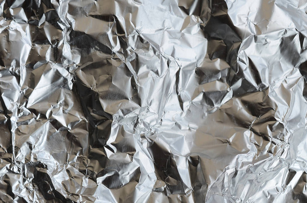 Thin wrinkled sheet of crushed tin aluminum silver foil background with shiny crumpled surface for texture - Foto, afbeelding