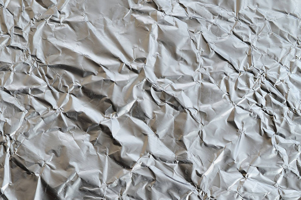 Тонкий морщинистый лист измельченного фонового материала из алюминиевой фольги с блестящей смятой поверхностью для текстуры
 - Фото, изображение