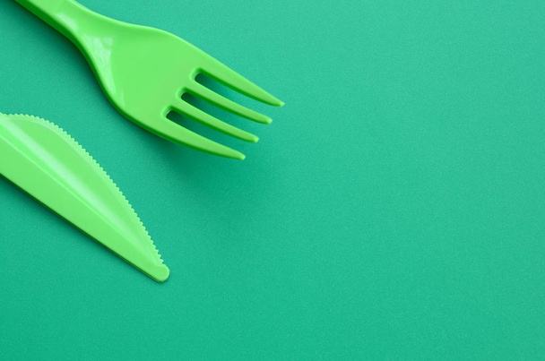 Plastic Wegwerpbestek groen. Plastic vork en mes liggen op een groene achtergrond oppervlak - Foto, afbeelding