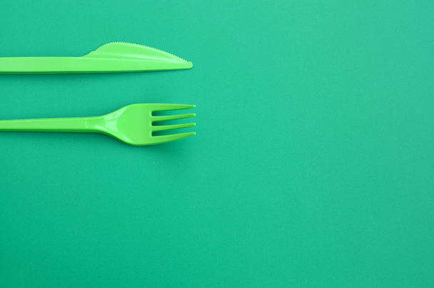 Disposable plastic cutlery green. Plastic fork and knife lie on a green background surface - Photo, image