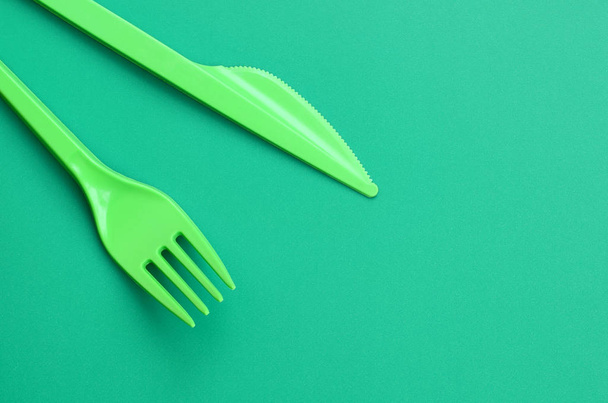 Cubertería de plástico desechable verde. Tenedor de plástico y cuchillo se encuentran en una superficie de fondo verde
 - Foto, Imagen