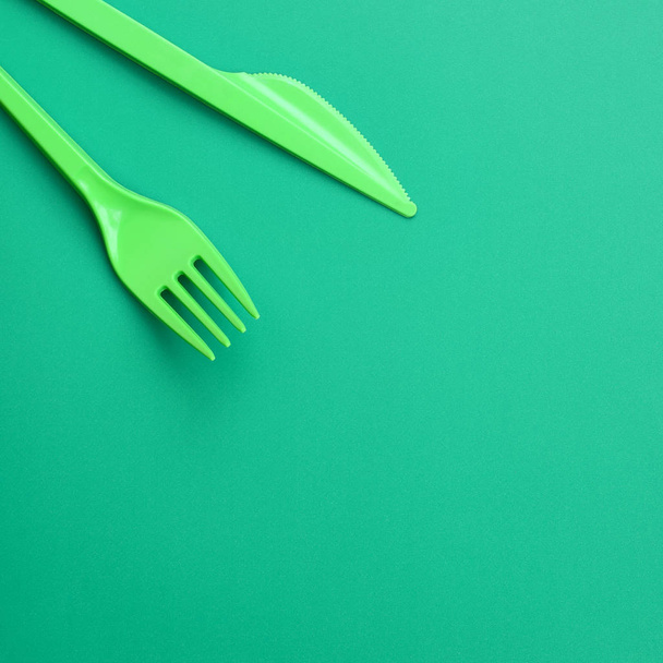Disposable plastic cutlery green. Plastic fork and knife lie on a green background surface - Fotó, kép