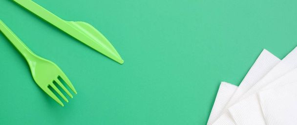 Μίας χρήσης Πλαστικά Μαχαιροπήρουνα πράσινο. Πλαστικό πιρούνι και μαχαίρι lie σε πράσινο φόντο επιφάνεια δίπλα από χαρτοπετσέτες - Φωτογραφία, εικόνα