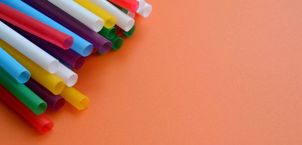 Many colorful straws for drinks lies on a bright orange background surface - Photo, Image