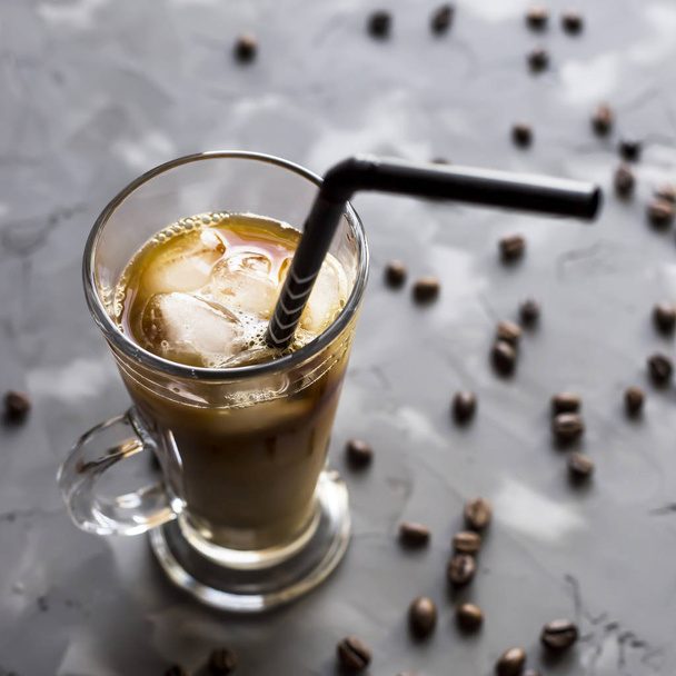 Czarna kawa zimna z lodem i mleka na szarym tle wśród ziaren kawy. W letnie napoje w filiżance szkła - Zdjęcie, obraz