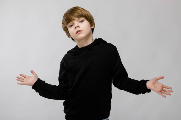 Lindo chico caucásico en traje negro mostrando diferentes expresiones en la pared blanca en el estudio
. - Foto, Imagen