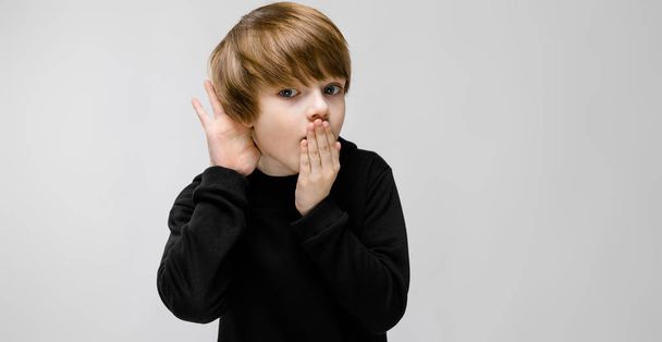 Aranyos kaukázusi fiú fekete ruhában, mutatja a különböző kifejezések fehér falon a stúdió. - Fotó, kép