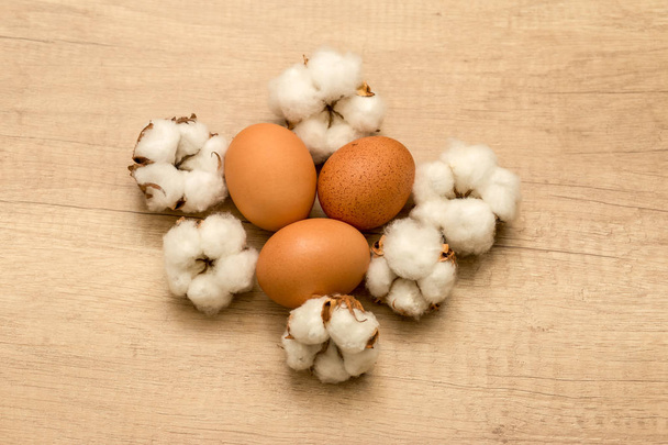 ωμά αυγά κότας και βαμβάκι ταξιανθίες σε φόντο ξύλινη - Φωτογραφία, εικόνα