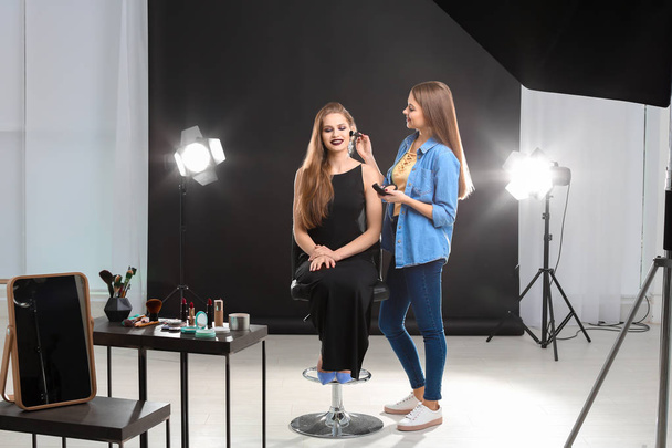 Professional makeup artist working with beautiful young woman in photo studio - Fotó, kép