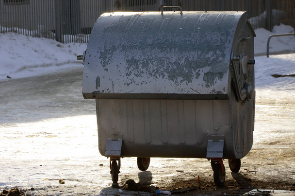 Een zilveren afval container staat in de buurt van residentiële gebouwen in de winter - Foto, afbeelding