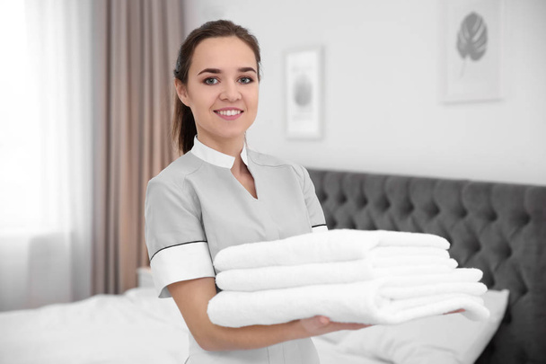 Young maid holding stack of towels in hotel room - Foto, Imagem