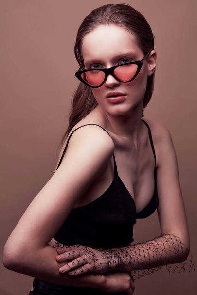 Fashion portrait of beautiful young woman in black bra, sunglasses with red lens, with massive earrings and veil on hand - 写真・画像