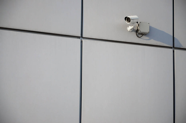 Біла камера спостереження, вбудована в металеву стіну офісного будинку
 - Фото, зображення