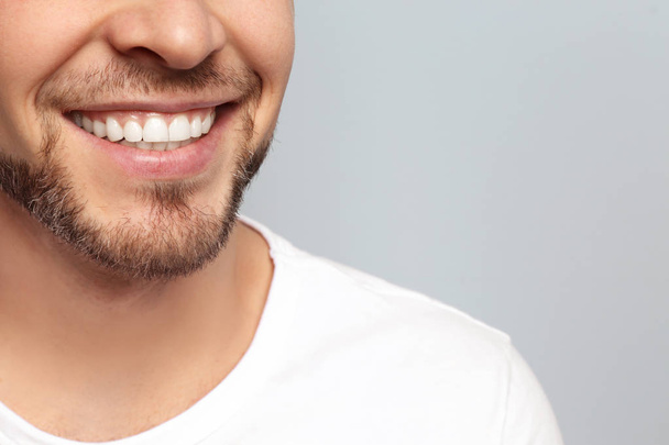 Young man with beautiful smile on grey background. Teeth whitening - Fotografie, Obrázek