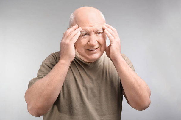 Senior man suffering from headache on light background. Enduring pain - Fotoğraf, Görsel