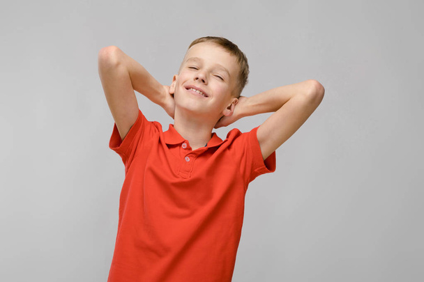 Cute blond caucasian preteen boy in bright t-shirt showing different expressions on white wall in studio. Holding hands behind the head with bliss. - Photo, Image