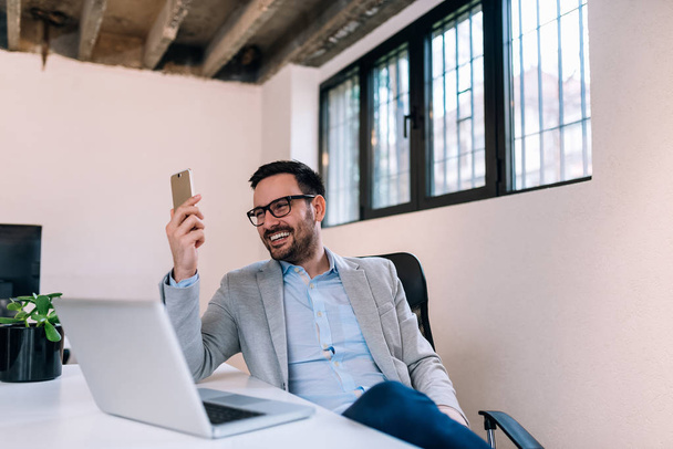 Portrait of smiling businessman reading message on smartphone in office. - Фото, зображення