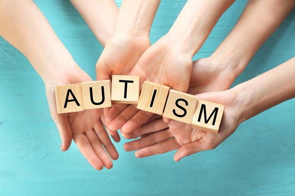Group of people holding cubes with word "Autism" on wooden background - Photo, image