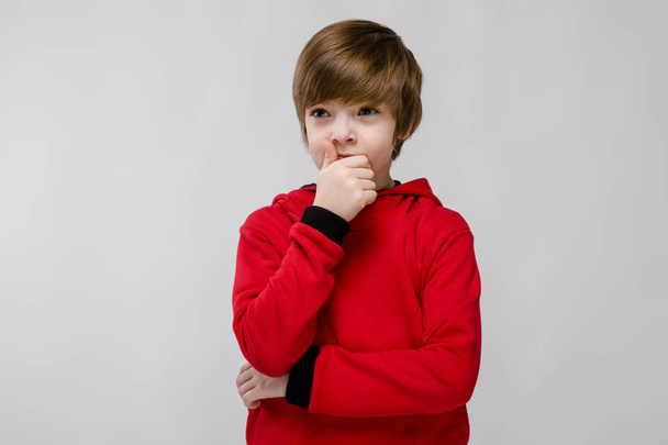 Nice preteen caucasian boy in casual outfit showing different expressions on white wall in studio. Looking at away thoughtfully with hand on chin. - Photo, Image