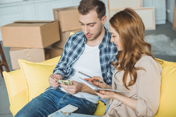 young couple taking notes and counting money while moving home - Photo, Image