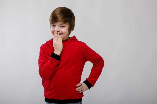 Szép, preteen kaukázusi fiú alkalmi ruhát mutatja a különböző kifejezések fehér falon a stúdióban. Vihogva, és amely a száját. - Fotó, kép