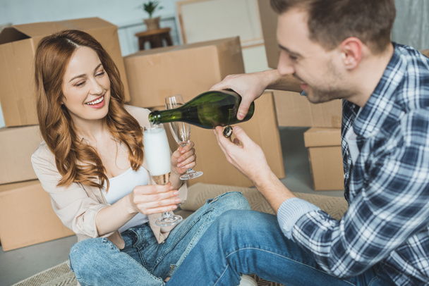 happy young couple celebrating relocation with champagne in new home - Photo, Image