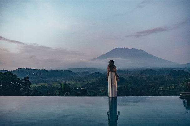 beautiful girl staying near swimming pool with fantastic volcano - Valokuva, kuva