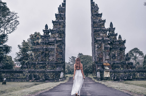 series traveling girl in Asia. Old indonesian gate. beautiful girl with long dark hair in elegant grey dress posing in beautiful nature place in Bali. - Photo, image