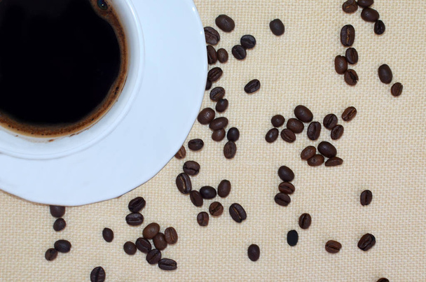 Біла чашка кави та кавові зерна на фоні натурального білизни. Постріл вище
 - Фото, зображення
