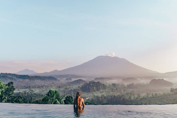 beautiful girl staying near swimming pool with fantastic volcano - Foto, Imagem