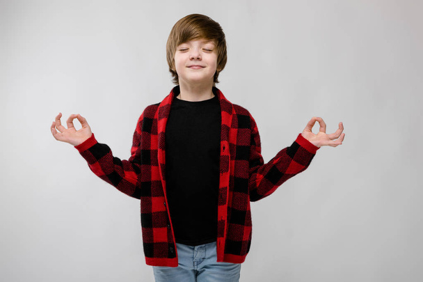 Nice preteen caucasian boy in casual outfit showing different expressions on white wall in studio. Holding hands like meditating. - Photo, Image