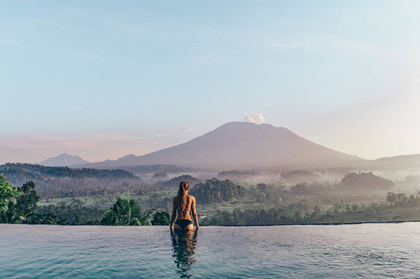 beautiful girl staying near swimming pool with fantastic volcano - Foto, afbeelding