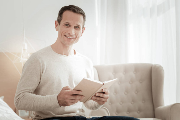 Satisfied smart man holding a book and smiling. - Fotoğraf, Görsel