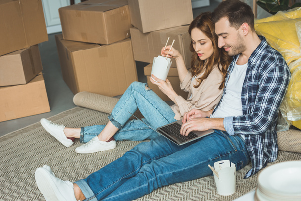 couple eating asian food while using laptop at new apartment, moving home concept - Photo, Image