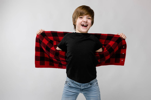 Nice preteen caucasian boy in casual outfit, stretching out his checkered shirt and showing different expressions on white wall in studio. - Photo, Image